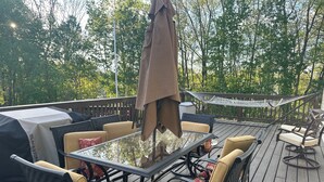 Eine Terrassenausstattung mit Tischplatte aus Glas, umgeben von Korbstühlen und floralen Kissen, einer Hängematte und einem Grill.