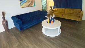 A living room with a blue sofa, a yellow sofa, a round coffee table, and a painting on the wall.