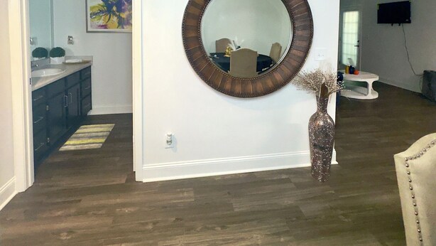 A spacious living area with a large mirror, wooden flooring, and a dining area visible through an open doorway.