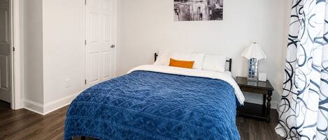A bedroom with a bed, a nightstand, a ceiling fan, a door, and a wall-mounted artwork.