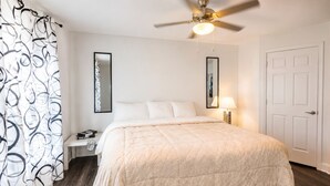 A bedroom with a bed, nightstand, lamp, ceiling fan, and a door.