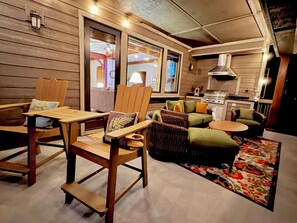 Un interior acogedor con paredes de madera, un comedor con sillas, un conjunto de sofás y una zona de cocina con una parrilla.