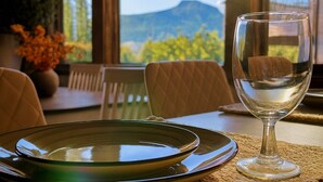 Een eettafel met een glas, een bord, een geweven placemat en een uitzicht op bergen door grote ramen.