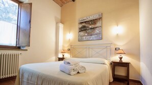 A bedroom with a bed, two bedside lamps, a radiator, and a window. - Two-room apartment of about 45 square meters with air conditioning and heating, tastefully furnished and composed of a living room with equipped kitchenette and sofa bed, bedroom with double bed and bathroom with shower and bidet.Located on the ground fl (Riparbella)