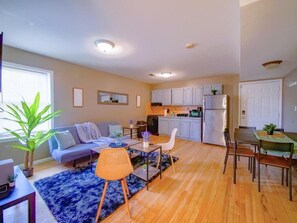 A compact living space with a sofa, dining table, chairs, a kitchen area, and a large window.
