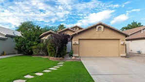 A residential house with a garage, a well-maintained lawn, and a stone pathway leading to the entrance. - Connect With Nature at This Beautiful Urban Farm (Mesa)