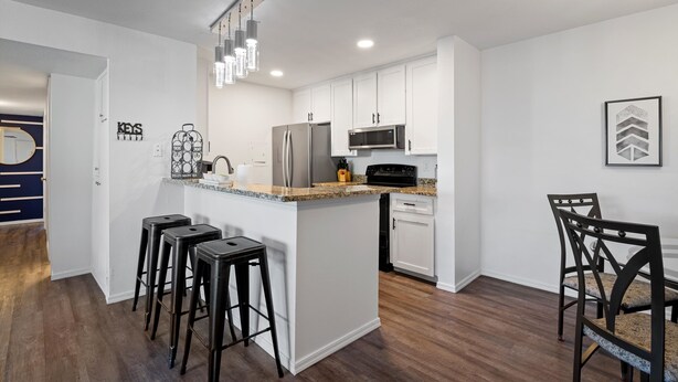 A modern kitchen with white cabinets, stainless steel appliances, and a granite countertop. There are two black bar stools and a dining table with chairs. - Connect With Nature at This Beautiful Urban Farm (Mesa)