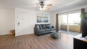 A living room with a grey sofa, a ceiling fan, a painting, and a sliding glass door to a balcony. - Connect With Nature at This Beautiful Urban Farm (Mesa)