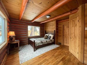 Ein Schlafzimmer in einer Blockhütte mit Bett, Nachttisch, Fenster und Holzwänden.