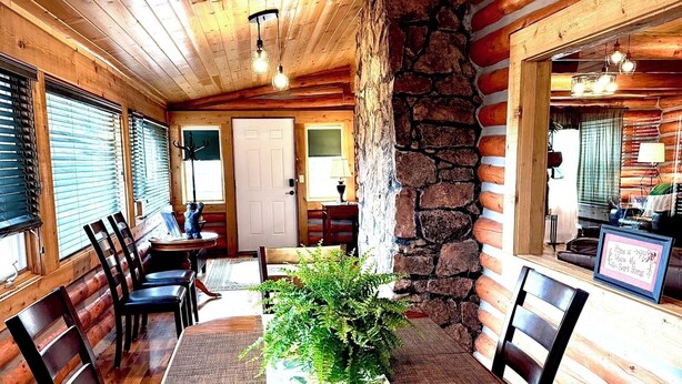 A dining area with a wooden table, chairs, and a stone wall. - Mountain Getaway Cabin steps from Dwtn. W.P.: Hike, Bike, Fish & Enjoy 338570 (Woodland Park)