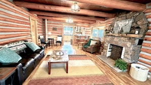 A log cabin interior with a fireplace, wooden walls, a sofa, a dining area, and a kitchen. - Mountain Getaway Cabin steps from Dwtn. W.P.: Hike, Bike, Fish & Enjoy 338570 (Woodland Park)
