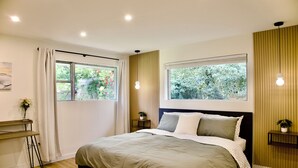 Un dormitorio con cama, dos mesitas de noche, una ventana con cortinas y vistas a zonas verdes.