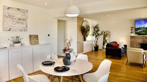 Una sala de estar moderna con chimenea, muebles blancos y un comedor con una mesa y sillas blancas.
