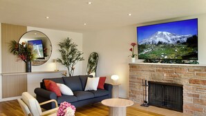 Una sala moderna con un sofá, una mesa de centro, una chimenea y un televisor grande montado en la pared.