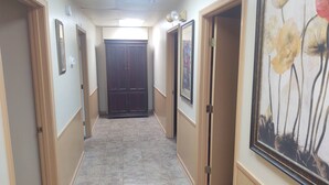 Un couloir avec des portes de part et d’autre, un sol carrelé et un luminaire au plafond.