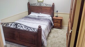 Un lit bien fait, avec une tête de lit et un pied de lit en bois, une table de chevet avec une lampe et un tableau encadré accroché au mur.