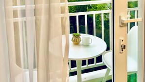 Un balcón con una mesa y sillas blancas, una planta pequeña en maceta y una taza blanca.