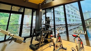 A gym with exercise equipment and large windows offering views of a residential building.