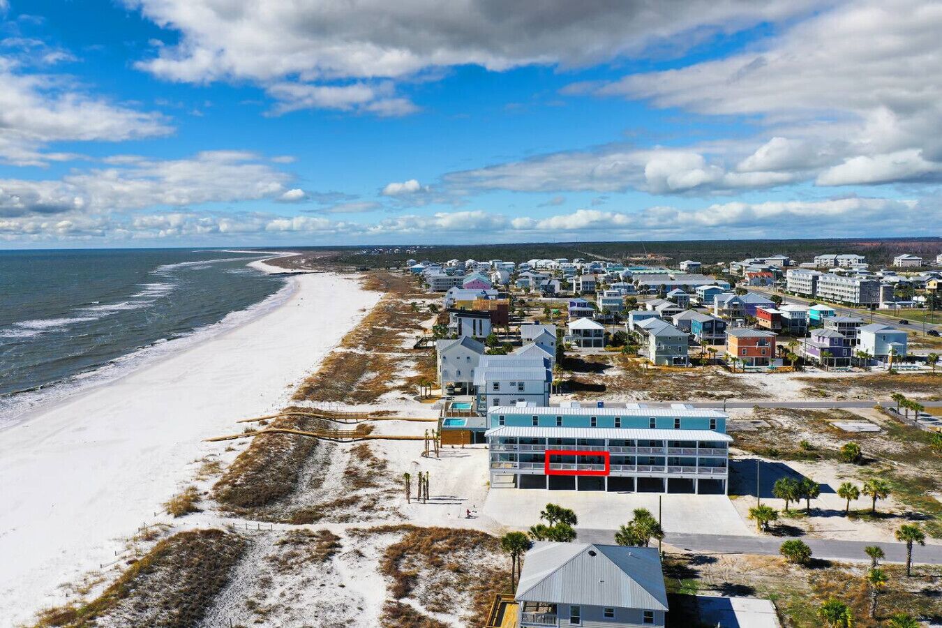 A coastal area with a beach, a row of houses, and a large building with a red sign.