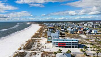 A coastal area with a beach, a row of houses, and a large building with a red sign.
