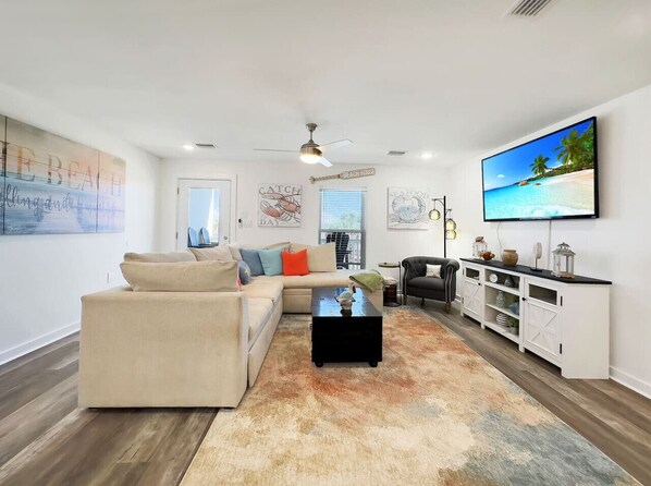 A modern living room with a beige sofa, a black coffee table, and a television on a white wall.