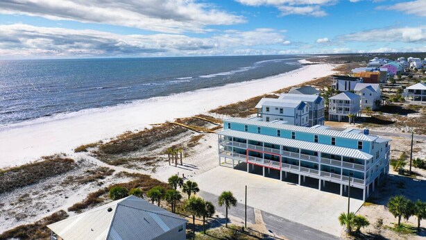 Een hotel aan de kust met uitzicht op het strand, bestaande uit een meerlaags gebouw met balkons, een zandstrand en een heldere lucht.