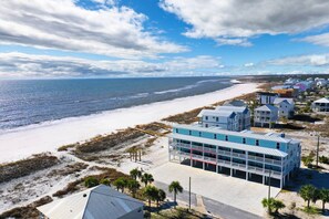 A coastal hotel with a beachfront view, featuring a multi-story building with balconies, a sandy beach, and a clear sky.