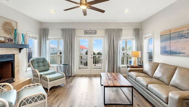 A spacious living room with a ceiling fan, wicker furniture, a leather sofa, and a view of the beach through large windows. - DuneFine Cape San Blas Sleeps 10 & Dog Friendly Private Pool (Cape San Blas)