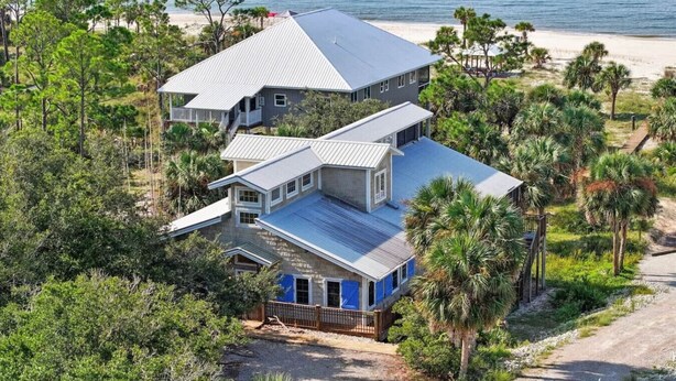 A large two-story house with a metal roof, surrounded by dense greenery and a beach in the background. - Charming Beachfront Beach House/2BR/Loft/Sleeps 8 (Cape San Blas)