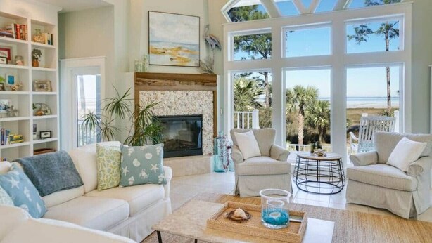Amplia sala de estar con chimenea, asientos cómodos y ventanas grandes con vista a la playa.