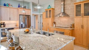 Una cocina moderna con encimeras de granito, electrodomésticos de acero inoxidable, armarios de madera e iluminación colgante.