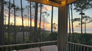 Un balcón con sofá y cojines, con vista a un área boscosa y una puesta de sol.