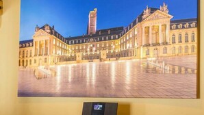 Fotografia emoldurada de um edifício histórico com uma torre central, exposta numa parede com superfície refletora abaixo.