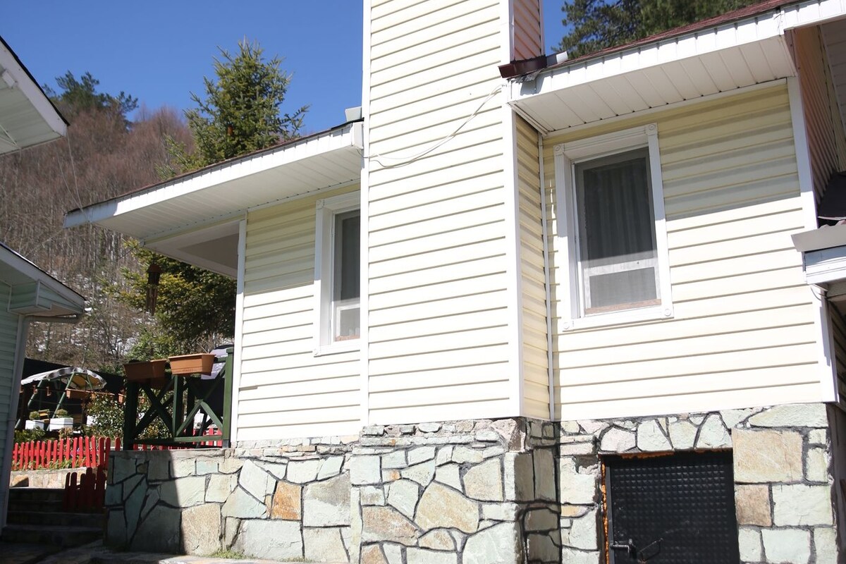 A two-story house with a stone foundation, a chimney, and a small porch.