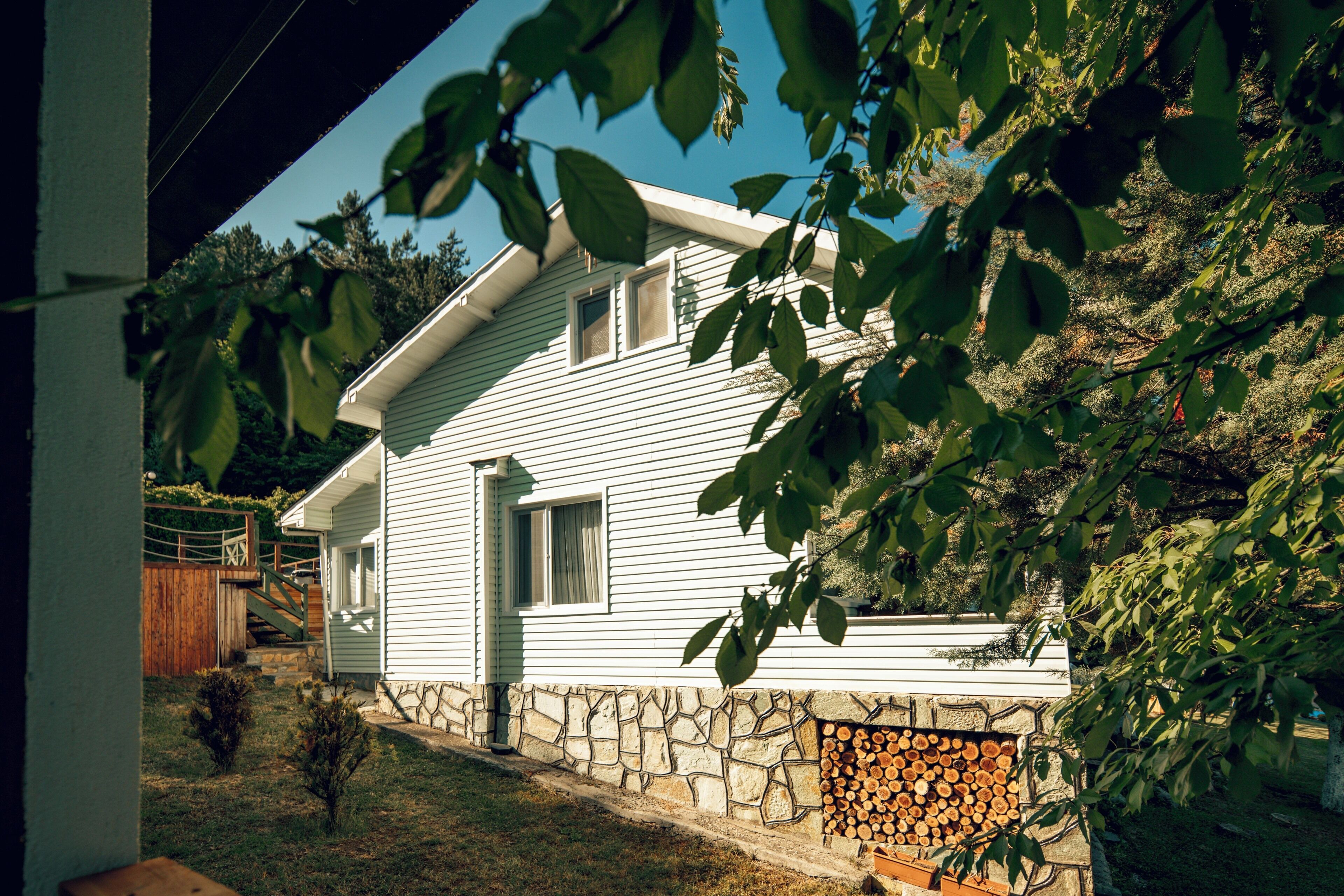A white house with a stone foundation, a small front yard, and a wooden fence.