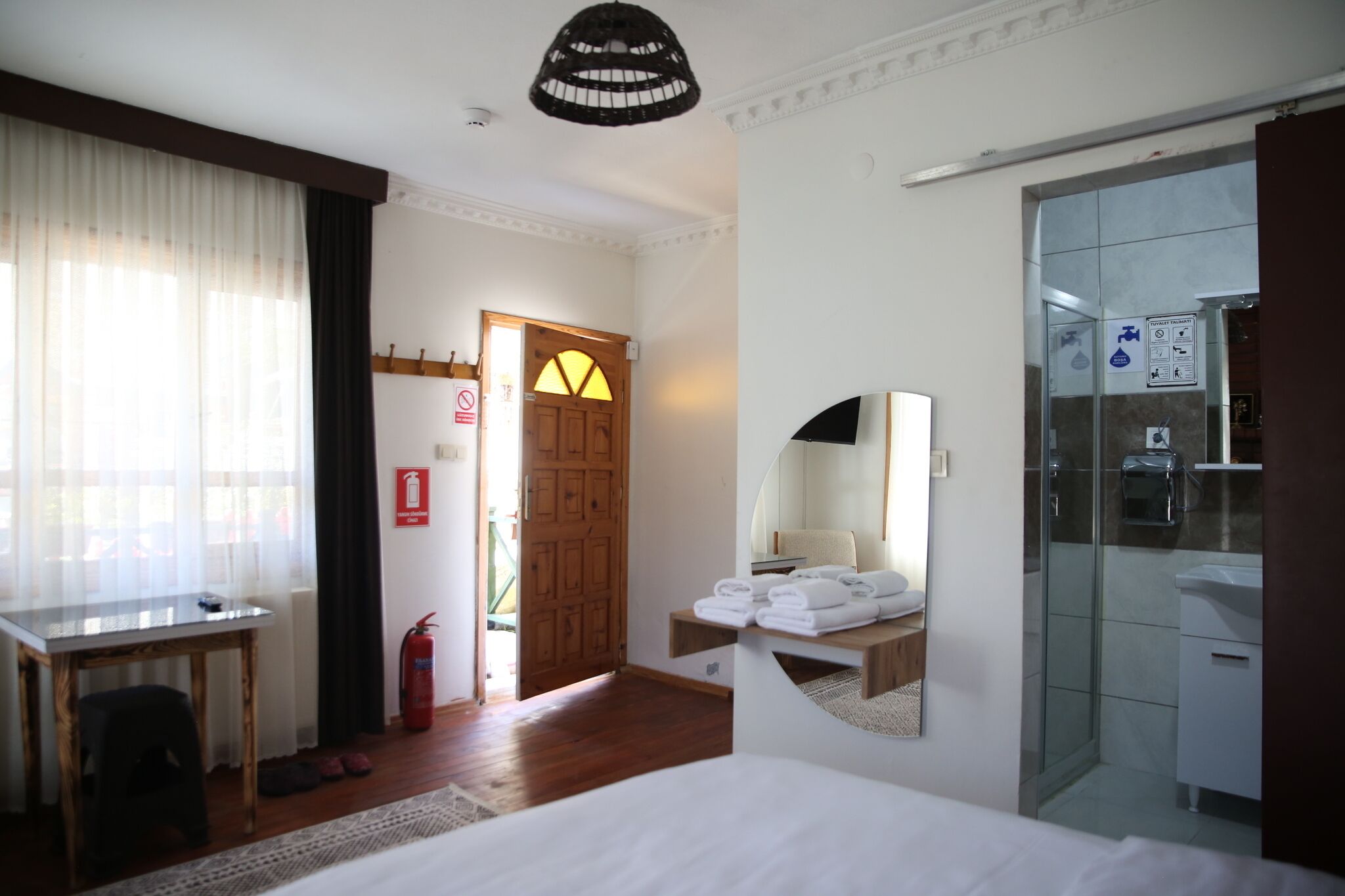 A hotel room with a bed, a desk, a mirror, a shower, and a door leading to the outside.