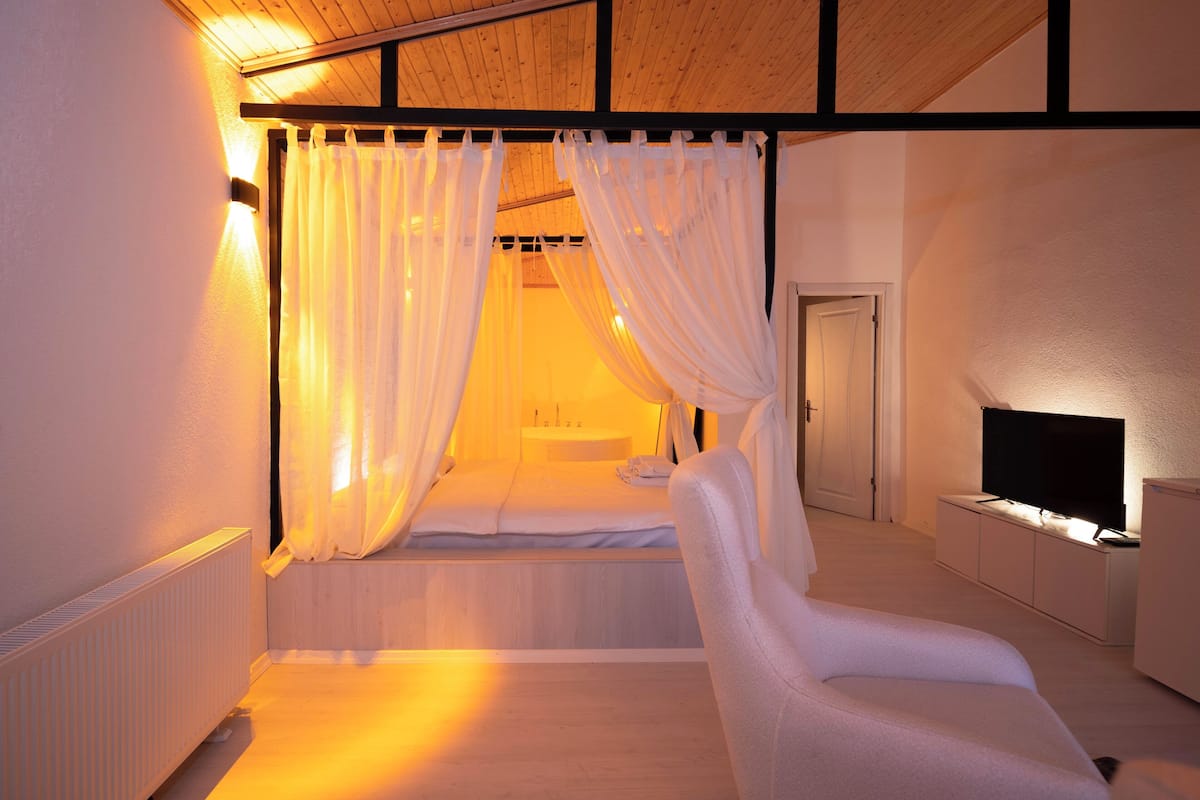 Un dormitorio con una cama, una silla, un televisor y una ventana con cortinas.