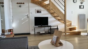 Ein modernes Wohnzimmer mit einer Holztreppe, einem Flachbildfernseher, einem runden Couchtisch und einem Bücherregal.