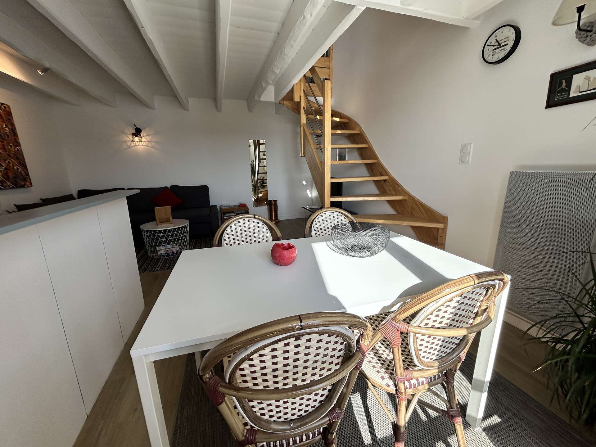 A dining area with a white table, wicker chairs, and a wooden staircase in the background.