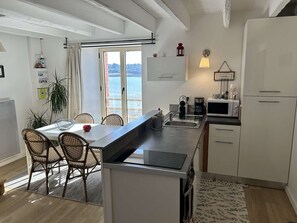 A modern kitchen with a large island, a dining area with wicker chairs, and a view of the sea through the window. - Harbour-view duplex in Erquy | 2 guests | Ref 515 (ERQUY)