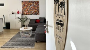 Ein modernes Wohnzimmer mit einem grauen Sofa, einem farbenfrohen abstrakten Gemälde und einem Surfbrett mit der Aufschrift 'California Surf Trip Southbay'.