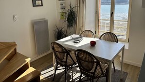 Ein Essbereich mit Tisch, Stühlen, einer Uhr, einer Lampe und Blick auf das Meer.