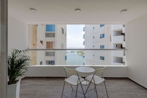 A balcony with a glass railing, two white chairs, and a potted plant.