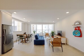 A modern living room with a sofa, dining table, chairs, a TV, and a refrigerator.