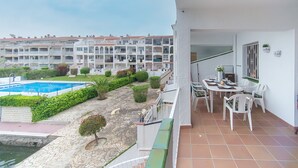Un balcone con vista su una piscina, un'area pranzo con sedie e tavolo, e un edificio a più piani sullo sfondo.