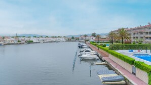Una marina con imbarcazioni ormeggiate lungo una passeggiata sul lungomare, fiancheggiata da edifici residenziali e un'area piscina.