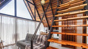 A modern living room with a grey sofa, a wooden staircase, and a large window with sheer curtains. - VILLA ESTORIL (Campina Grande Do Sul)