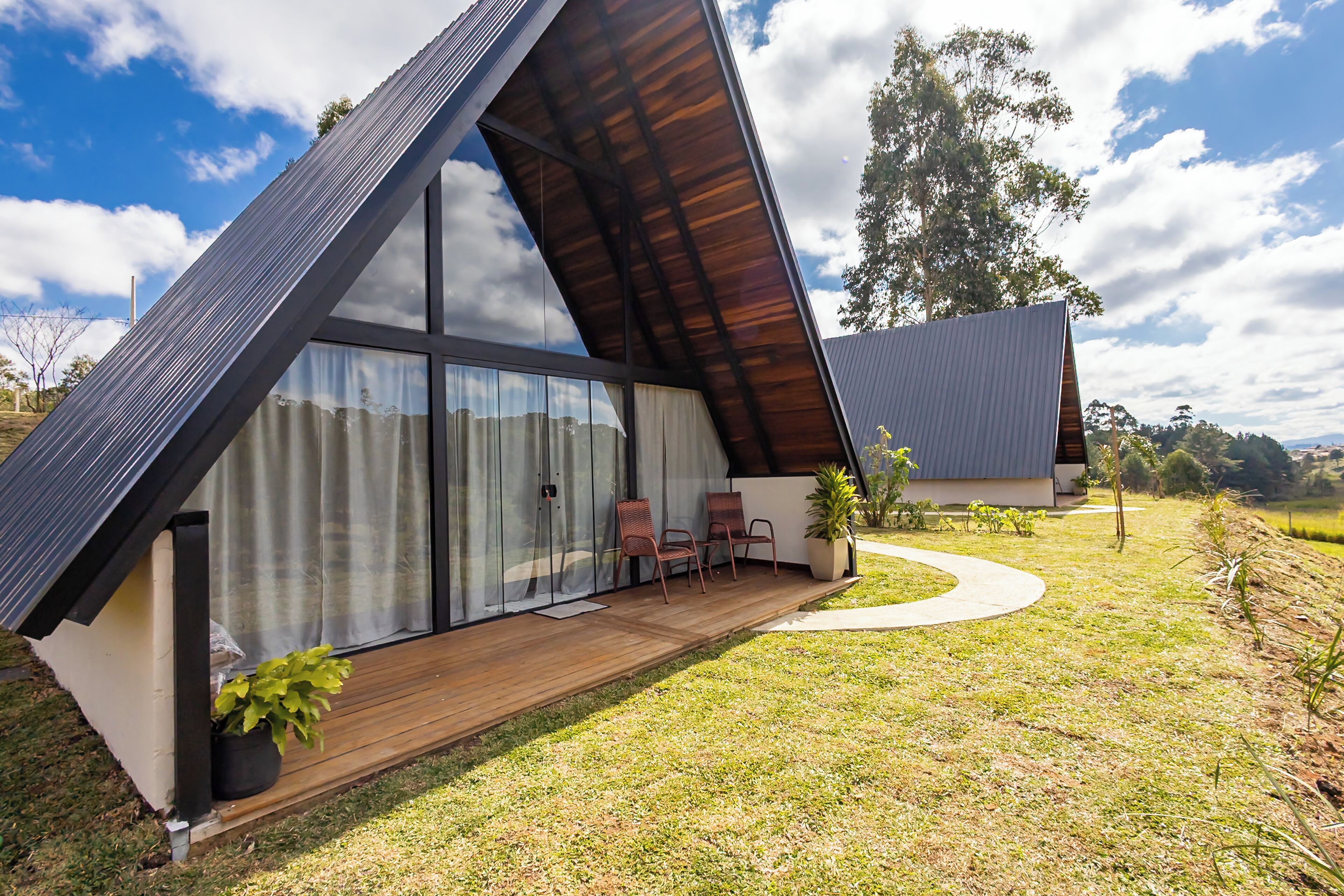 A modern house with a sloped roof, large glass windows, and a wooden deck with two chairs.