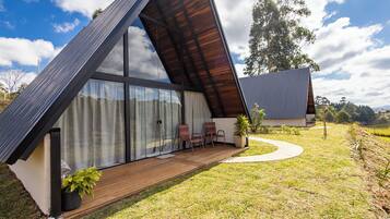 A modern house with a sloped roof, large glass windows, and a wooden deck with two chairs.