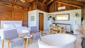 A spacious room with a large bed, a sitting area with a table and chairs, a kitchen area, and a large bathtub. - VILLA ESTORIL (Campina Grande Do Sul)